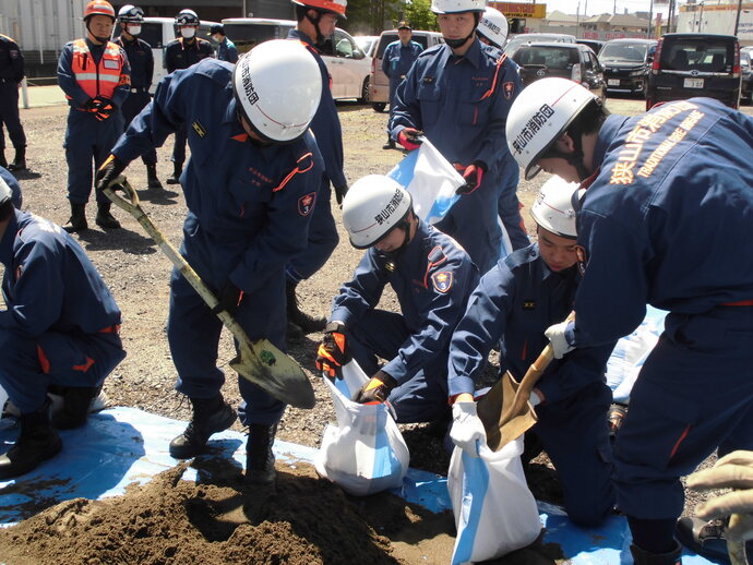 消防団員が協力して、スコップで土を土のう袋に入れている様子