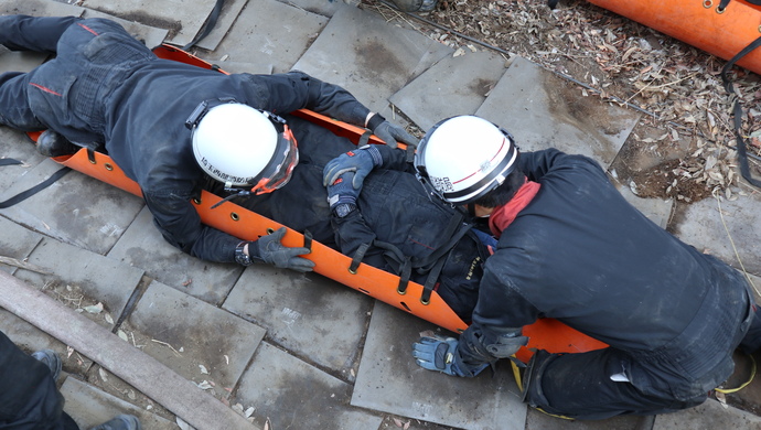 隊員2名が連携して要救助者1名を収容したスケッドストレッチャーのベルト固定を実施している写真